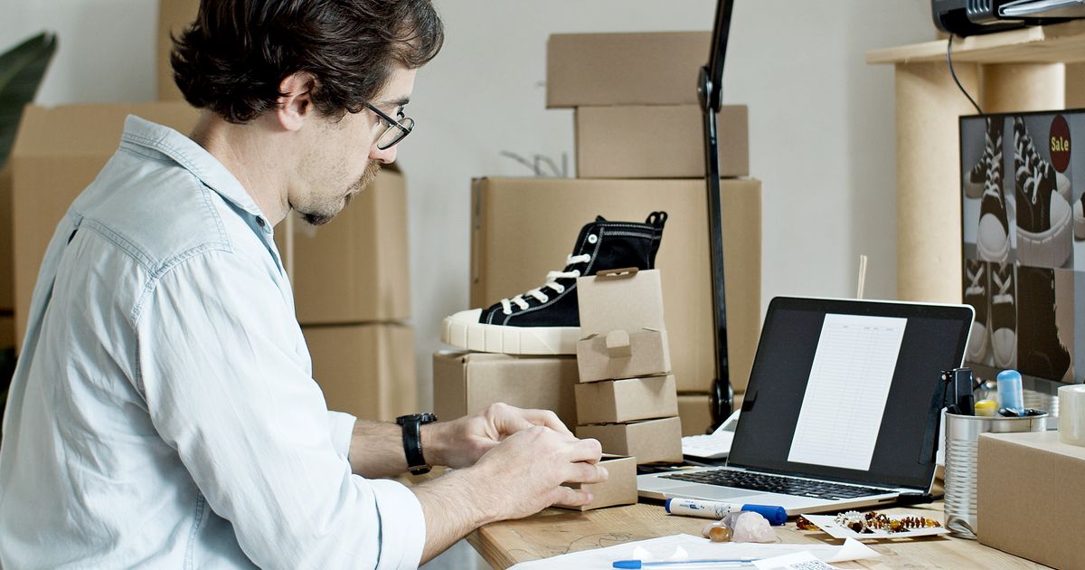 A small business owner preparing customer parcels beside a laptop.