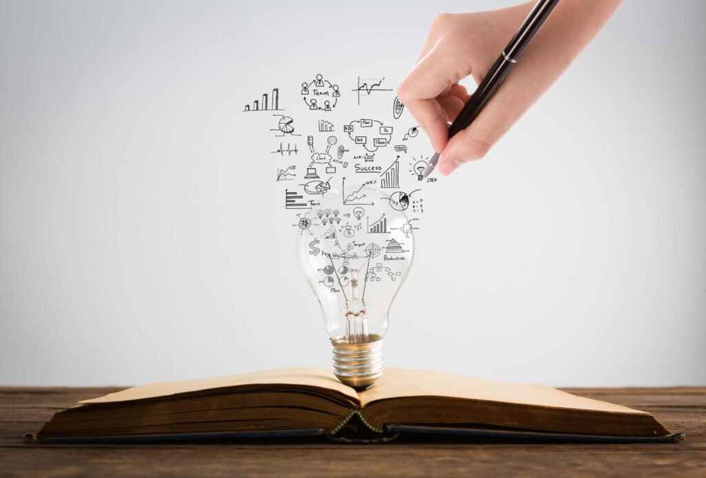 Turning Ideas Into Insight Hand drawing business strategy icons inside a light bulb over an open book, symbolizing data-driven research and strategic insights.